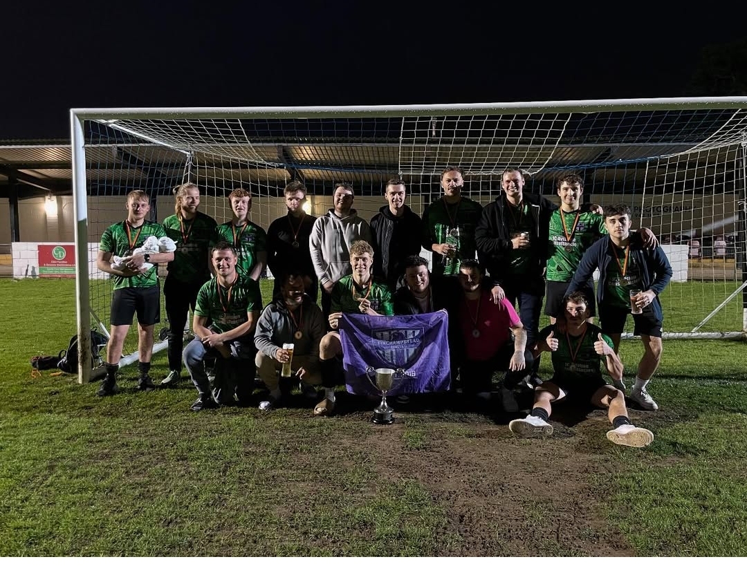 Finchampstead United full squad with the cup and medals in front of the goal under floodlights